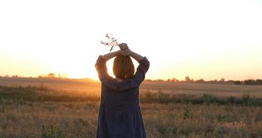 jeune femme rousse dans une belle robe bohème se relaxant sur le terrain pendant le coucher du soleil brumeux, femme à l'extérieur avec bouquet dans les mains