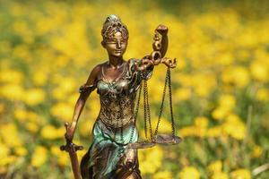 statue de thémis contre une pelouse de pissenlits. symbole de la justice et du droit, du crime et du châtiment. photo