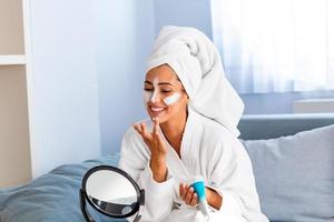 si belle. gros plan d'une fille avec un masque de beauté sur son visage regardant dans le miroir. la fille utilise un masque naturel. jolie jeune femme assise avec un masque facial sur sa peau photo