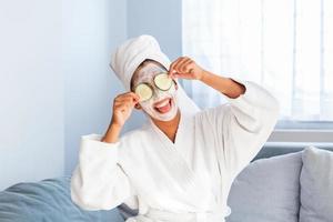 belle jeune femme avec un masque facial sur son visage tenant des tranches de concombre frais. soins et traitement de la peau, spa, beauté naturelle et concept de cosmétologie photo