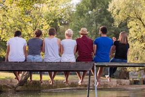 vue arrière d'amis appréciant la pastèque assis sur le pont en bois photo