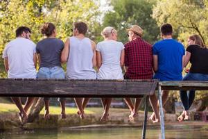 vue arrière d'amis appréciant la pastèque assis sur le pont en bois photo