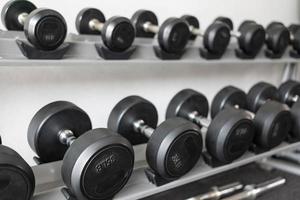 debout avec des haltères. salle de sport et de remise en forme. équipement de musculation. ensemble d'haltères noires, de nombreux haltères sur rack dans un centre de remise en forme sportive photo