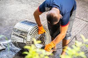 bangkok thaïlande - 6 juin 2022. le bricoleur lave une machine à laver en retirant le tambour et en le lavant avec un tuyau haute pression. personne portant des gants orange tout en travaillant habilement. photo