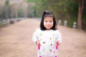 jolie fille asiatique sont de doux sourires, portant des chandails blancs pour se promener dans le parc naturel. l'enfant pousse le chariot rose sur un chemin de terre marron. concept d'enfants apprenant la nature autour. bébé a 3 ans. photo