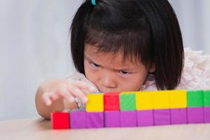 enfant petite fille jouant des jouets en bois à la maison ou à l'école maternelle. l'enfant trie et construit sérieusement les blocs de bois, elle vise les blocs de jouets à assortir. concept d'enfants perfectionnistes. photo