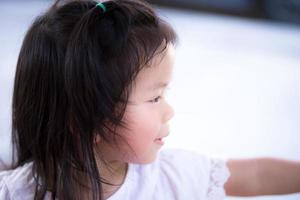 gros plan vue latérale petit sourire doux enfant mignon. candide fille asiatique heureuse. enfants âgés de 3 à 4 ans portant une chemise blanche. elle joue devant la maison. photo