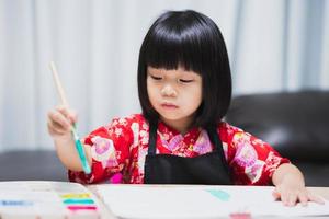 petite fille asiatique intelligente ayant une idée de faire de l'art comme passe-temps à la maison. apprentissage et éducation de l'enfant. enfant faisant de l'artisanat pour l'école à la maison dans la classe de cours. bébé de 4 à 5 ans porte une chemise rouge. photo