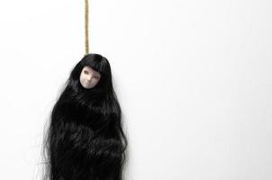 poupée fantôme femme asiatique aux cheveux longs suspendue avec la corde agissant se suicider sur fond blanc. concept effrayant minimal d'halloween. photo