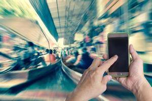 main tenant un téléphone intelligent mobile avec un arrière-plan flou du marché flottant photo