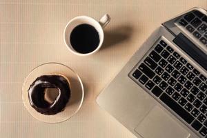 vue de dessus d'ordinateur portable avec une tasse de café et un beignet sur la table. photo