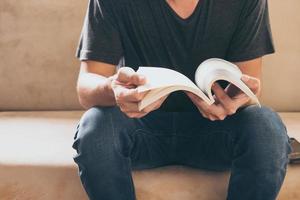 gros plan d'un jeune homme décontracté assis sur un canapé et lisant un livre à la maison. photo