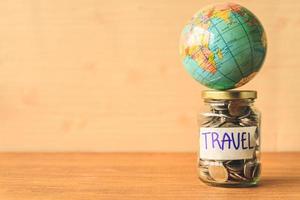 pièces de monnaie dans un bocal en verre avec étiquette de voyage et globe sur table en bois. économiser de l'argent pour le concept de voyage. espace libre pour le texte photo