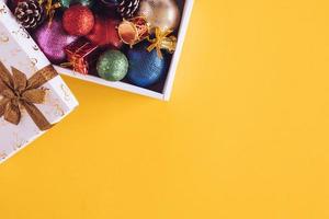 décorations de noël dans une boîte cadeau sur fond jaune. espace libre pour le texte photo