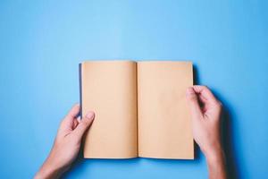 vue de dessus des mains tenant un livre vierge prêt avec un espace de copie prêt pour le texte sur fond bleu. photo