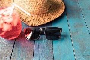 chapeau avec lunettes de soleil et cocktail rouge sur fond de planche de bois peint en bleu. notion de vacances d'été