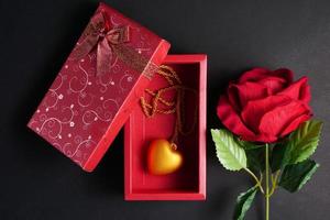 rose rouge avec collier coeur en or dans une boîte cadeau rouge sur fond noir. concept de saint valentin. photo