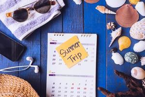 vue de dessus du calendrier avec accessoires pour voyage d'été et coquillages sur fond de planche de bois peint en bleu.