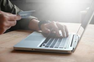 technologie, shopping et concept bancaire - gros plan d'un homme décontracté tenant une carte de crédit et utilisant un ordinateur portable sur la table, tonique avec la lumière du soleil photo