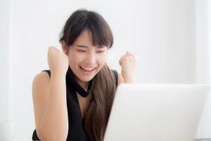 beau portrait asiatique jeune femme sourire travaillant en ligne ordinateur portable avec heureux satisfait assis sur le bureau, fille utilisant un ordinateur portable avec excité et heureux, concept d'entreprise et de réussite.