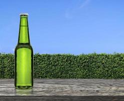 bouteille de bière avec des gouttes d'eau sur une terrasse de table en bois avec une texture de mur d'herbe verte et un ciel bleu vif