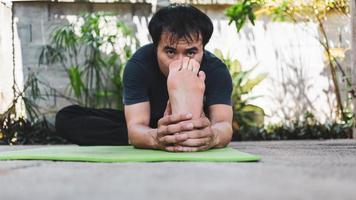 concept de vie sain de jeune homme asiatique pratiquant le yoga. assis en position assise, penché en avant, les mains aux pieds. janusirasana pose sur un tapis de yoga vert.mode de vie sain photo