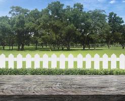 terrasse de table en bois avec, clôture en bois blanche et buisson vert sur fond de ciel bleu clair photo