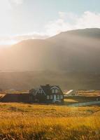 maison en bois islandaise qui brille de la lumière du soleil sur le pré et les oiseaux qui volent au coucher du soleil l'été au village de pêcheurs d'arnarstapi, islande photo