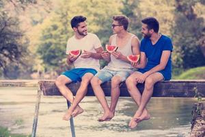 hommes appréciant la pastèque assis sur le pont en bois photo