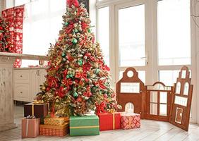 le sapin de noël est décoré de jouets rouges et verts, de boîtes de cadeaux au sol. ambiance du nouvel an dans la maison, intérieur festif. photo