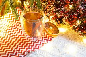 gobelet en verre transparent à double paroi avec thé chaud et bâtons de cannelle sur la table avec décor de noël. ambiance de nouvel an, tranche d'orange séchée, guirlande et guirlande, branche d'épicéa, cosy photo