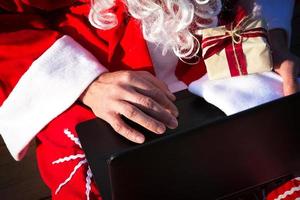 le père noël avec un ordinateur portable et un cadeau à la main. commandez des cadeaux pour Noël et le nouvel an via la boutique en ligne. réserver les services d'un animateur pour les vacances. photo