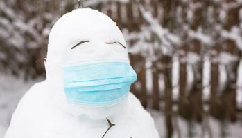 bonhomme de neige dans un masque médical - une nouvelle réalité, protection contre la maladie, l'infection, la vie dans l'épidémie de covid. les mains des femmes mettent un masque de bonhomme de neige. activités de plein air en famille en hiver photo