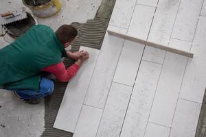 travailleur installant les carreaux en céramique effet bois sur le sol photo