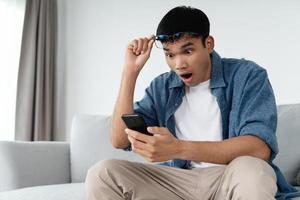 portrait d'un homme asiatique excité regardant un téléphone portable, homme recevant de bonnes nouvelles à l'aide d'un smartphone à la maison. photo