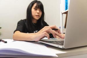 Une adolescente asiatique utilise la technologie de l'ordinateur portable sur Internet, des informations de recherche en ligne, un réseau social et des devoirs d'éducation sur la table. photo