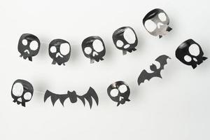 crânes et chauves-souris volantes découpées dans du papier noir sur fond blanc, préparation pour halloween. photo