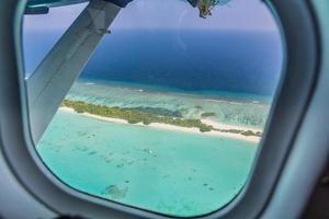 fenêtre d'avion avec vue magnifique sur l'île des maldives. fond de tourisme de voyage de vacances d'été de luxe, vue depuis la fenêtre de l'avion. atolls et îles avec une mer tropicale incroyable