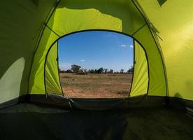 voyageur vert tente camping voyage en plein air. vue depuis la tente à l'intérieur sur le soleil bleu du ciel dans le paysage d'été. le soir de la journée propice au sommeil et au repos du corps