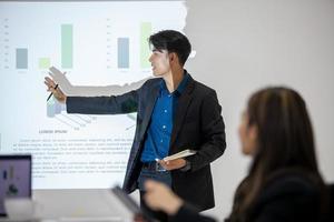 des collègues masculins et féminins de l'équipe commerciale asiatique qui parlent au travail partagent des idées avec un tableau à bord, de jeunes collègues de présentation heureux travaillent ensemble à bord. photo