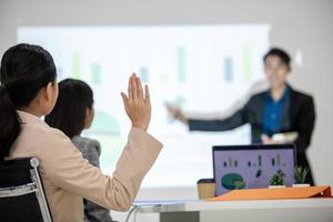 équipe commerciale asiatique collègues masculins et féminins parlant au travail partagent des idées avec un tableau à bord, les collègues ont levé la main pour poser des questions. photo