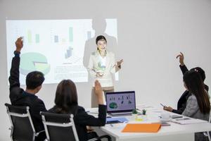 équipe commerciale asiatique collègues masculins et féminins parlant au travail partagent des idées avec un tableau à bord, les collègues ont levé la main pour poser des questions. photo