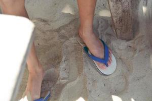 les pieds de quelqu'un qui se tient sur le sable et porte des tongs blanches et bleues. photo