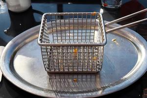 friteuse métallique vide sur une table avec quelques petits morceaux de frites. photo