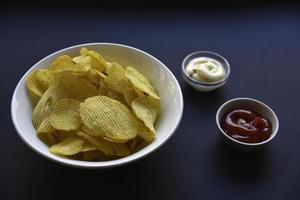 délicieuses chips de pommes de terre avec des sauces sur fond noir. apéritif de croustilles avec sauce. restauration rapide sur fond noir. photo