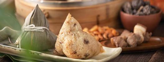 boulette de riz - nourriture chinoise zongzi dans un bateau à vapeur sur une table en bois avec mur de briques rouges, fond de fenêtre à la maison pour le concept de festival de bateaux-dragons, gros plan. photo