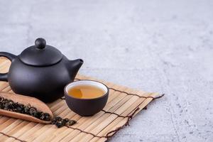 thé chaud dans une théière noire et des tasses et des feuilles de thé sèches sur fond de ciment gris clair, gros plan, concept de conception d'espace de copie.