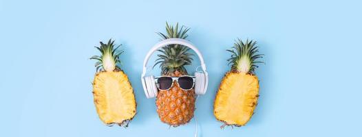 ananas drôle portant un casque blanc, concept d'écoute de musique, isolé sur fond coloré avec des feuilles de palmier tropicales, vue de dessus, design plat. photo