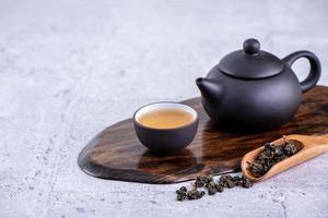 thé chaud dans une théière noire et des tasses et des feuilles de thé sèches sur fond de ciment gris clair, gros plan, concept de conception d'espace de copie. photo