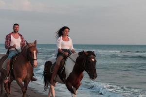 un couple d'amoureux en vêtements d'été à cheval sur une plage de sable au coucher du soleil. mer et coucher de soleil en arrière-plan. mise au point sélective photo